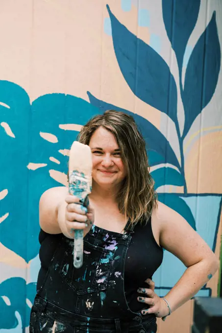 smiling woman holding out a paintbrush covered in paint