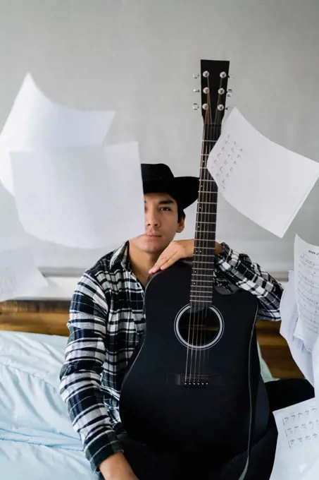 Latin man with  guitar on bed with note sheets floating around