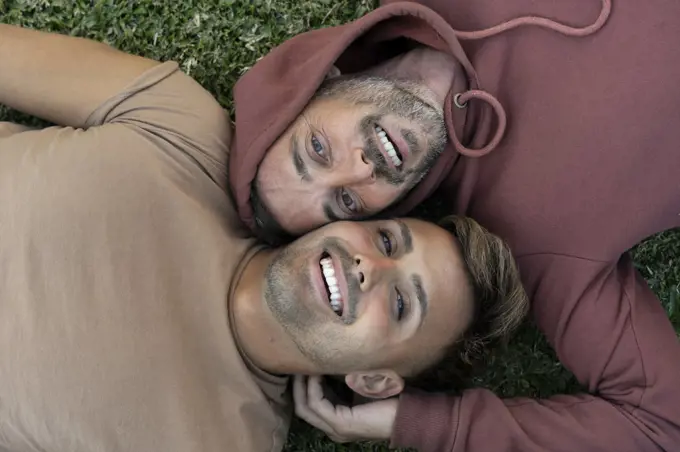 Top view of a male gay couple lying on the grass, looking at camera