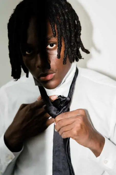 Black man with dreadlocks wearing a suit fixing his tie