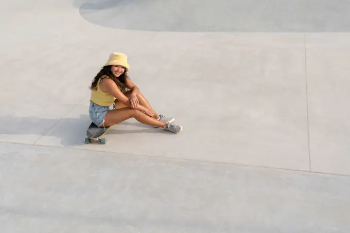Asian woman sitting on her skateboard in the skate park smiling
