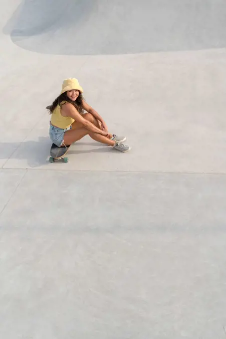 Asian woman sitting on her skateboard in the skate park