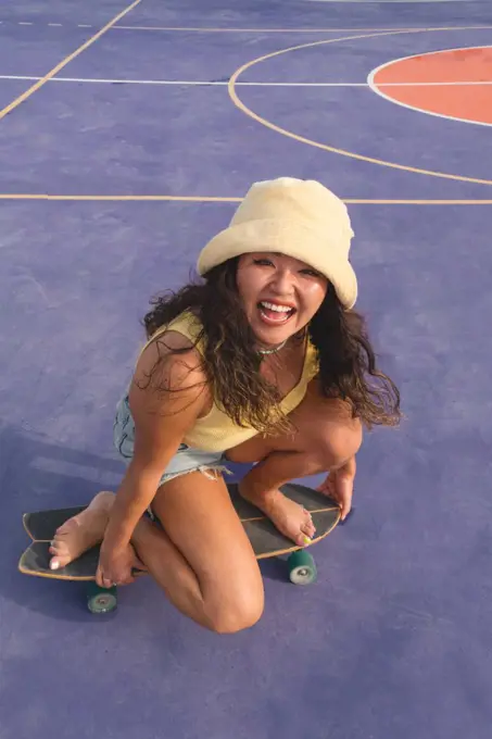 Asian woman sitting on her skateboard on the purple background