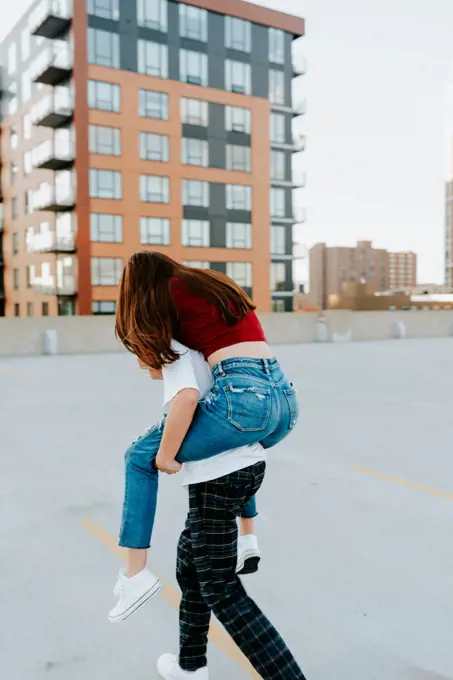 girl on boy's back as they run on a rooftop in downtown