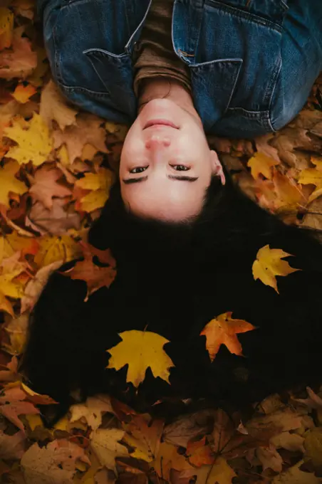 Asian Japanese young woman in jean jacket lays in fall leaves