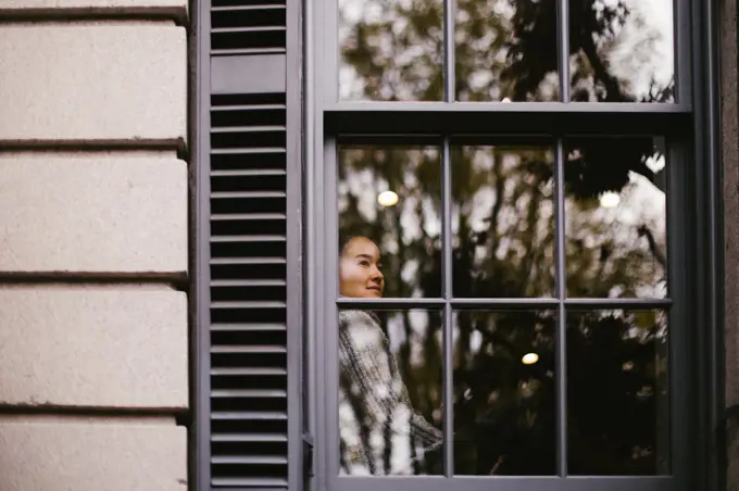 Asian woman gazes contentedly outside window from comfortable house