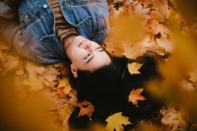 Asian woman lies in pile of fall orange and yellow leaves