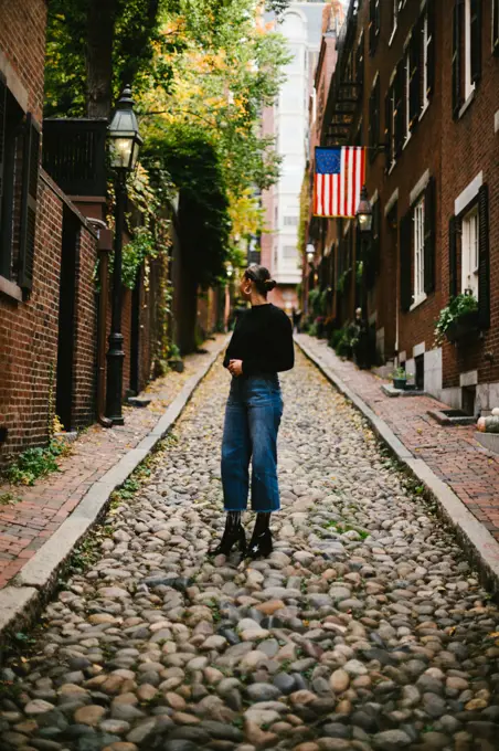 Woman on cobblestone road with American flag from brick townhouse