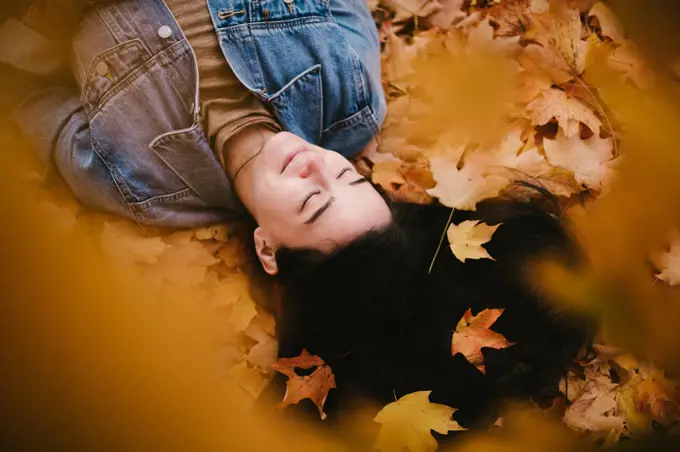 Japanese asian woman lays in pile of leaves with calm eyes closed
