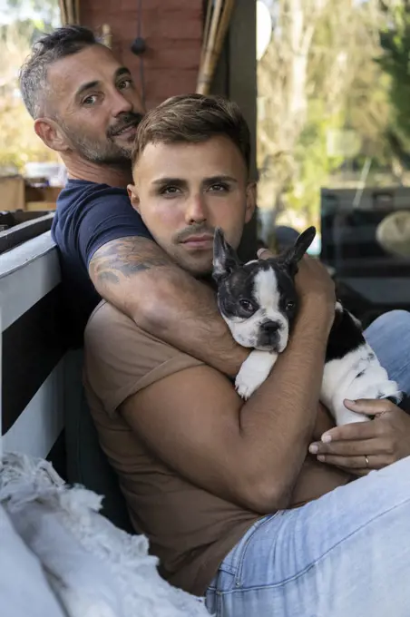 Gay male couple hugging while holding their French Bulldog