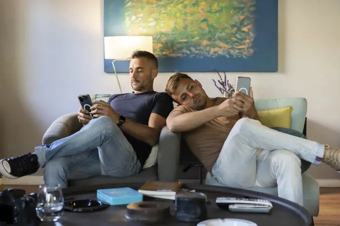 Gay couple relaxing on the couch while using smartphones