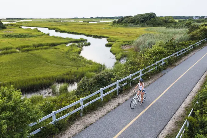 Aerial drone of Woman biking through Cape Cod Marshes bike path
