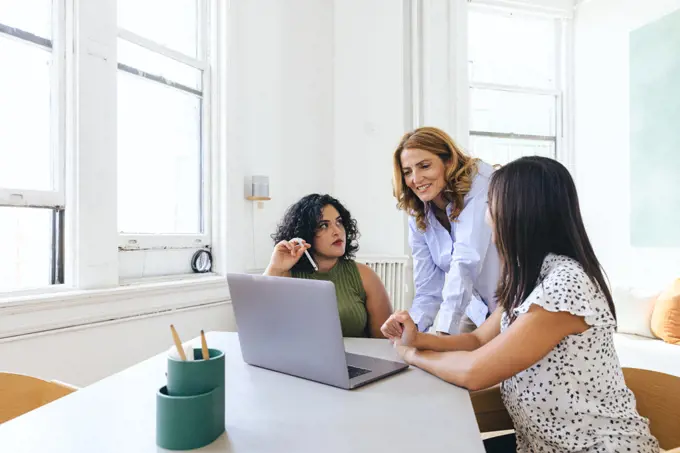 Female colleagues discussing over laptop during meeting