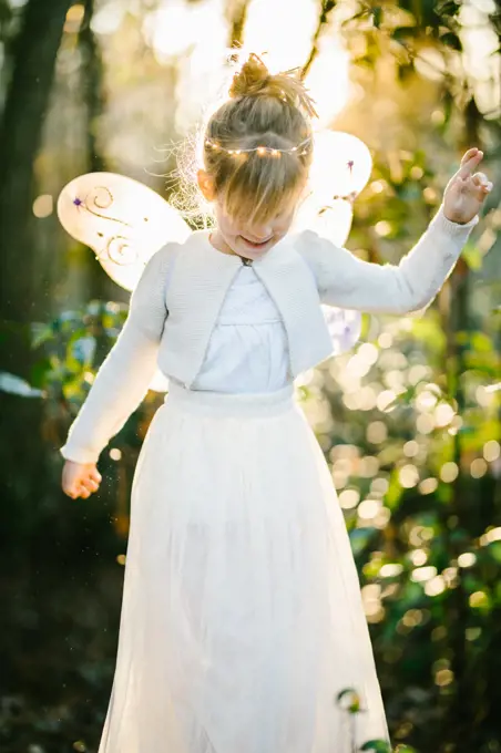 Girl in angel wings with light shining through forest with bokeh