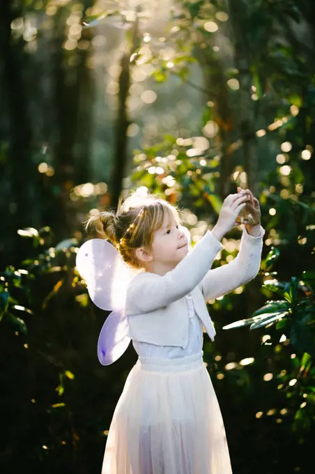 Girl in white angel dress with wings in shining light in forest