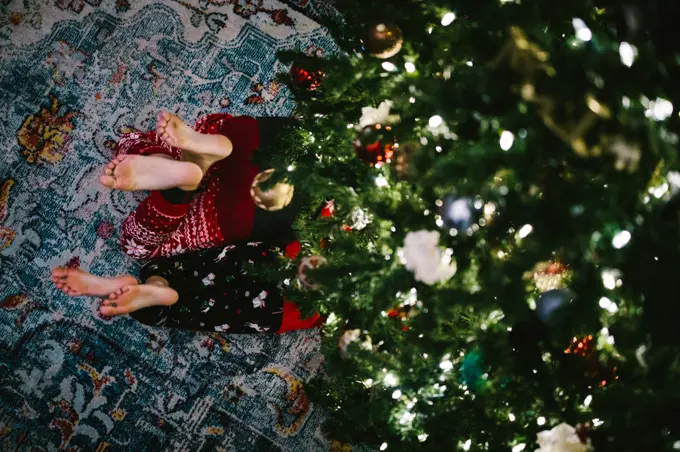 Feet of children siblings poke out from under decorated Christmas tree