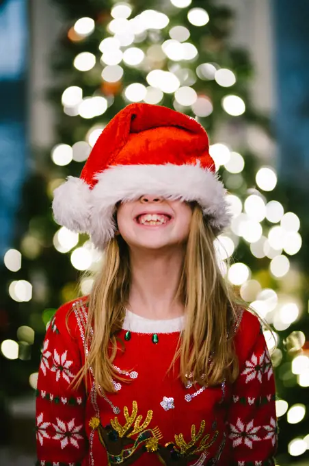Blond child smiles big in santa hat in front of Christmas tree
