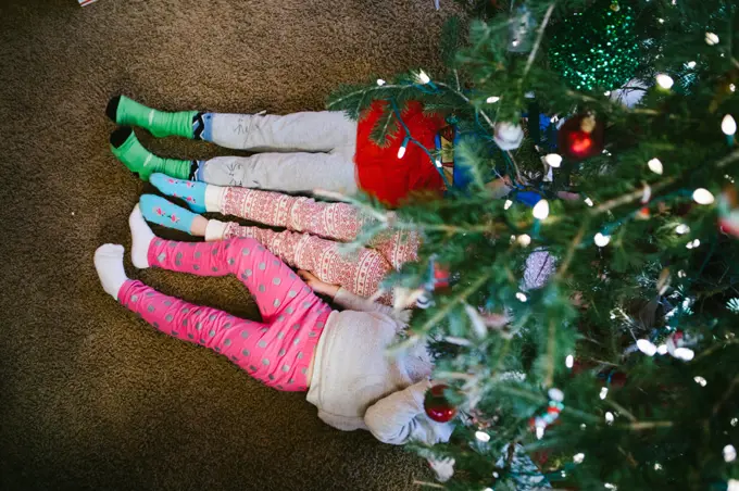 Siblings snuggle under the tree in Christmas pajamas