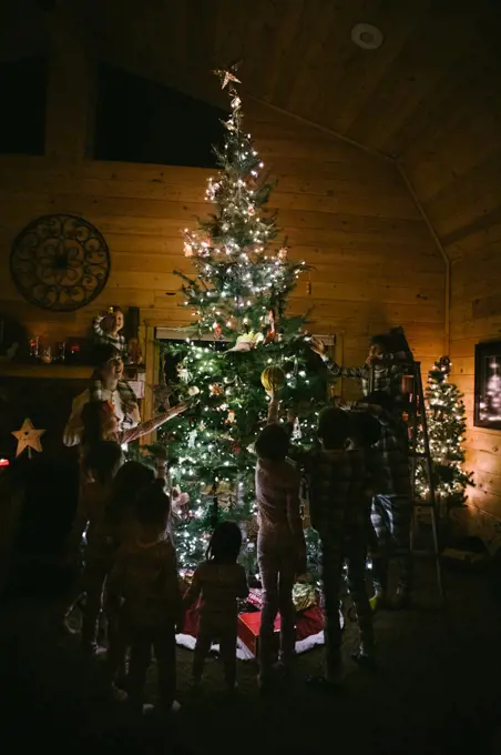 Kids decorate Christmas tree in cabin with ornaments in pajamas