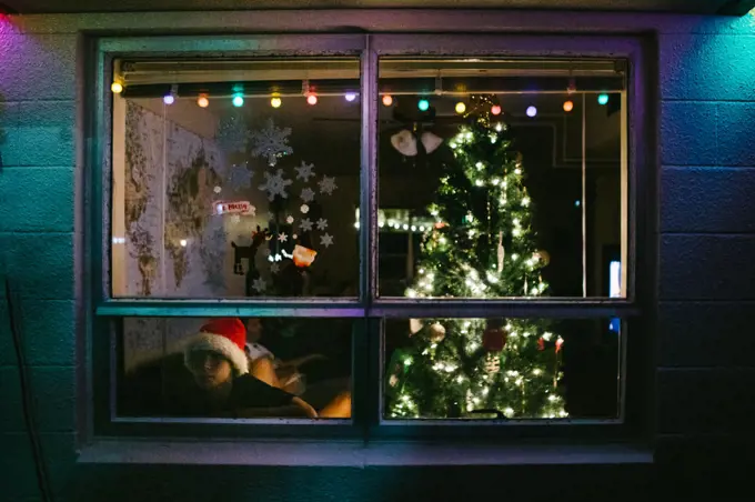 Boy looks out window of home with Christmas tree and Santa hat