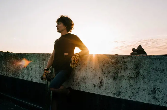 portrait of man standing in the sunset with his skateboard