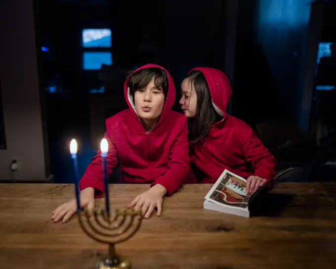 Two playful children sit together at table with Hannukah menorah