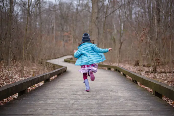 A child in bright colorful clothes runs down path in woods