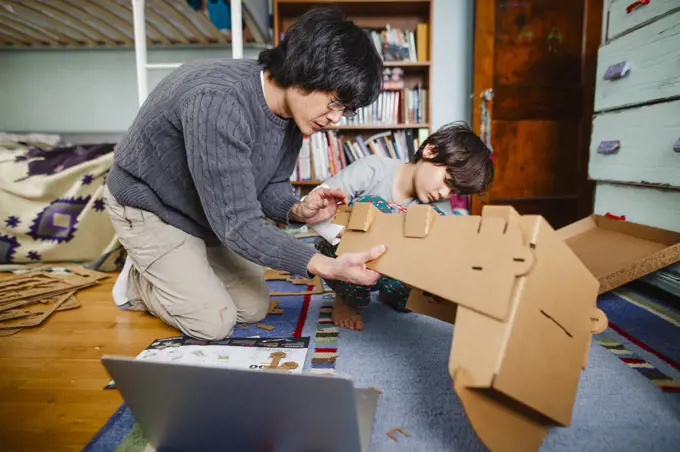 A dad and son build structure together with cardboard