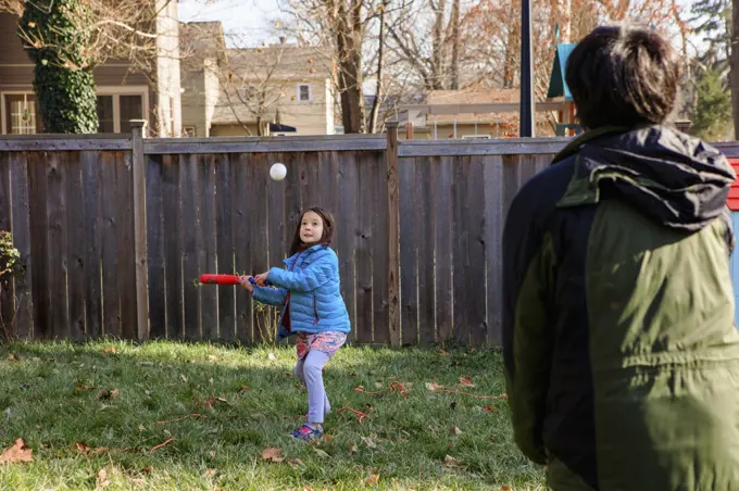 A little girl plays softball with father in backyard in winter