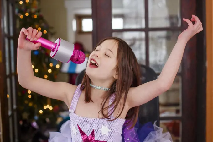 A girl with a pink microphone and tutu joyfully sings alone