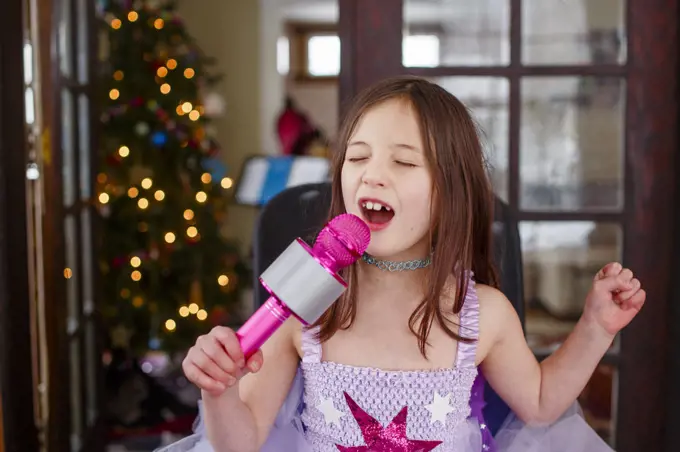 a little girl in costume sings loudly into a microphone at home