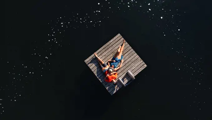 Couple laying together on swim platform on lake in summer.