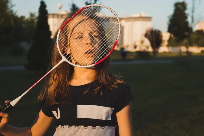Portrait of girl looking through badminton racket at the park