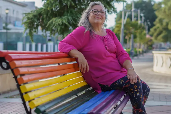 woman  sitting on a bench painted in the colors of the LGBT flag.
