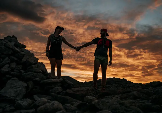 couple holds hands in front of colorful sunrise, Katahdin, Maine