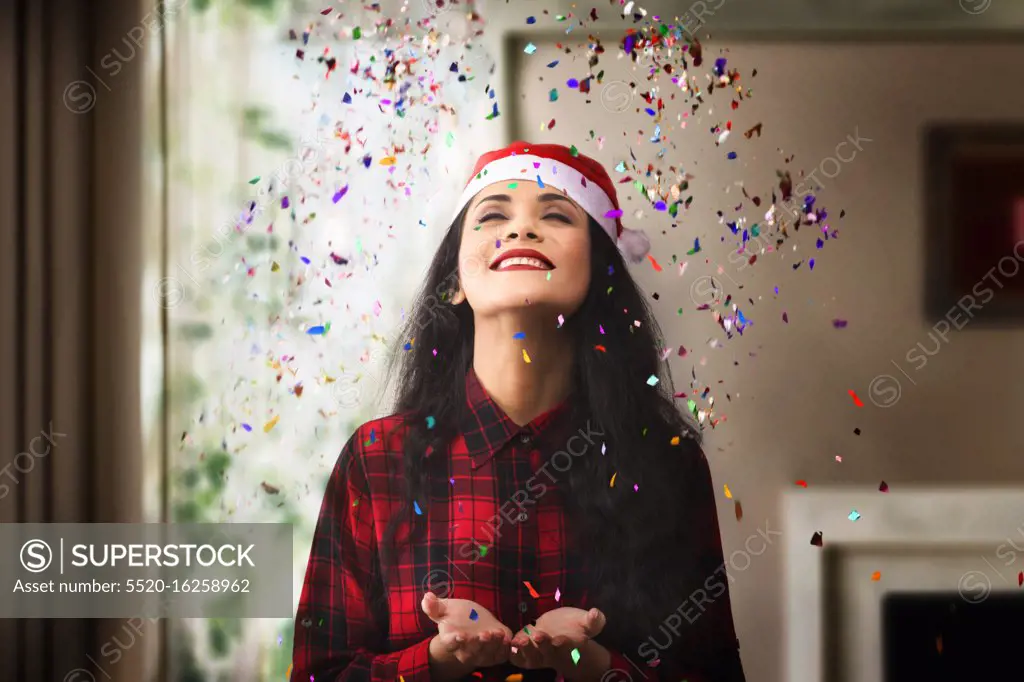 Portrait of a young woman throwing confetti at home during Christmas celebration.
