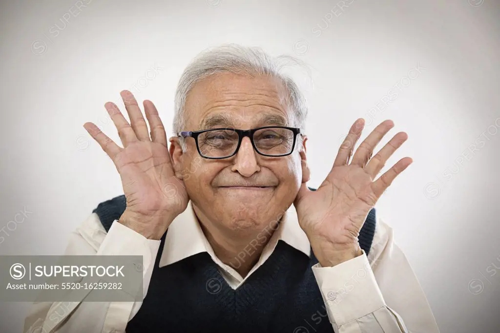 Old man making funny face with hands in his ears - SuperStock