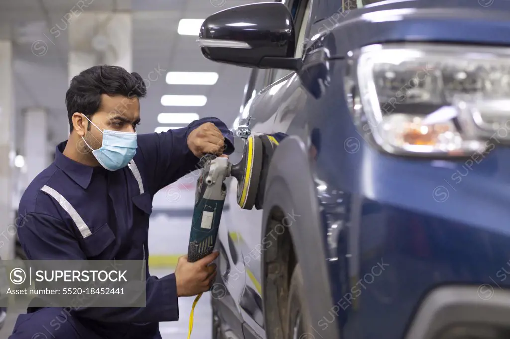 mechanic polishing a car with an electric orbital polisher in auto repair Shop