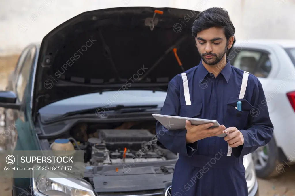 A MECHANIC USING A DIGITAL TABLET TO CHECK THE WORKING OF A CAR