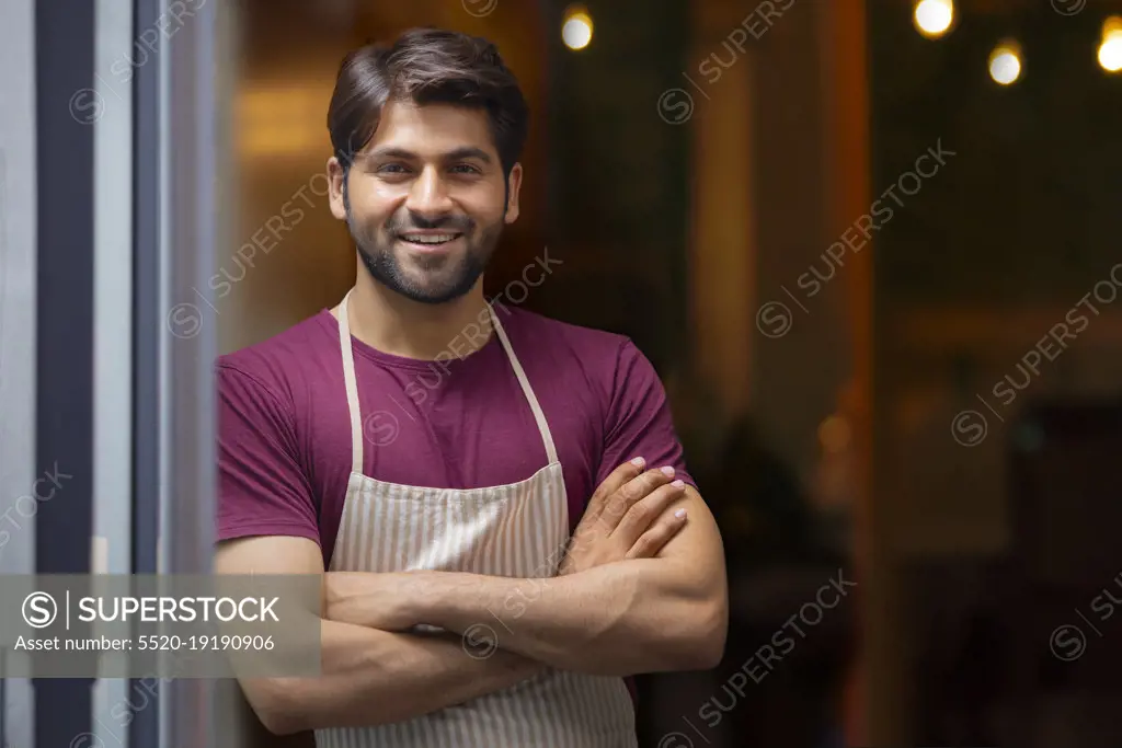 A WAITER HAPPILY LOOKING AT CAMERA AND POSING WHILE IN RESTAURANT