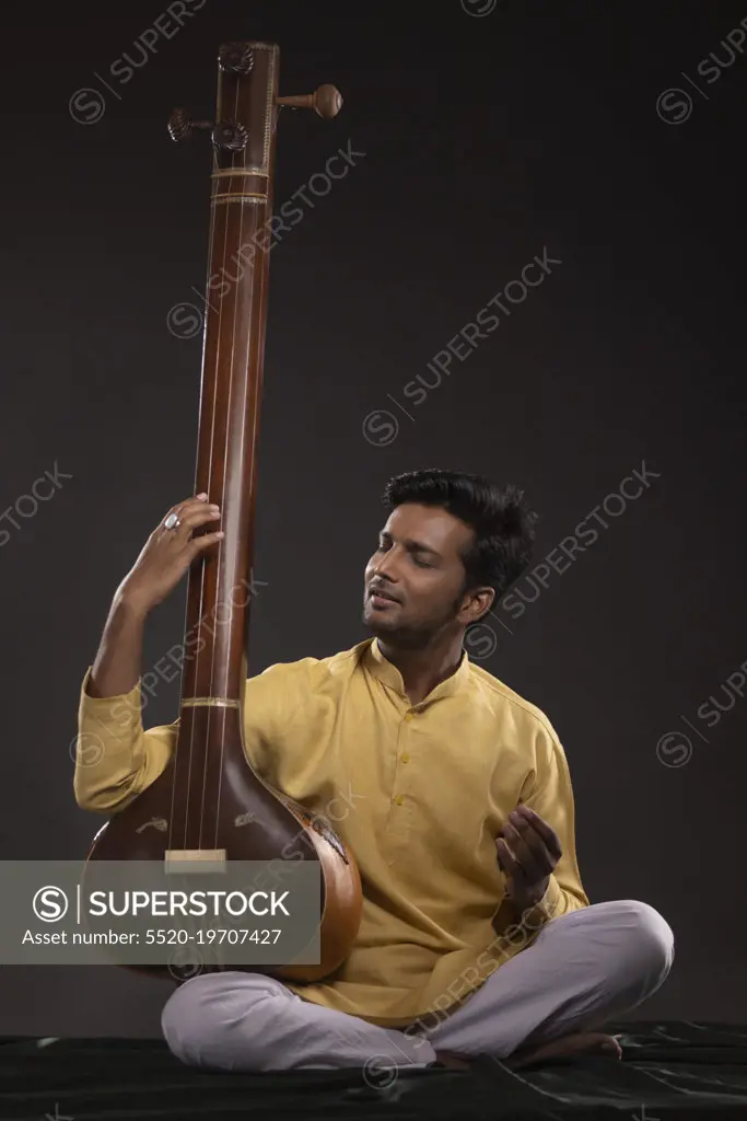 Portrait of young man performing with Tanpura at concert