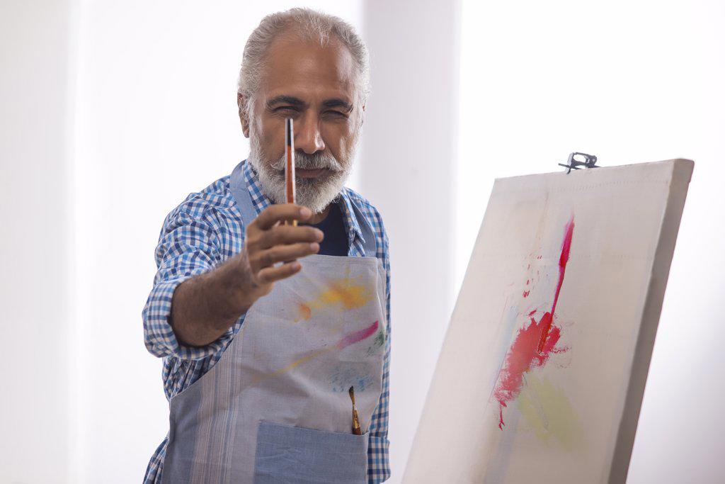 AN OLD MAN POSING IN FRONT OF CAMERA WITH PAINTBRUSH IN HAND