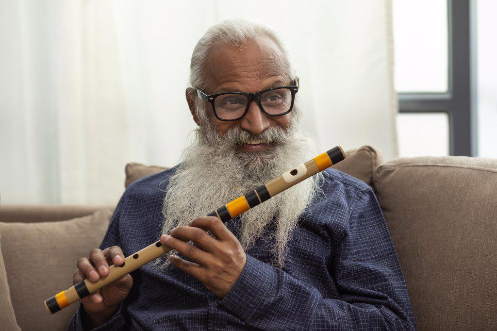 A BEARDED OLD MAN SMILING WHILE PLAYING FLUTE