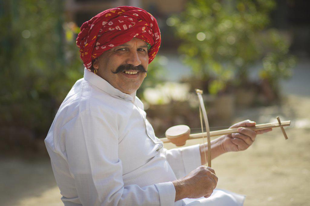 A SENIOR ADULT VILLAGER LOOKING AT CAMERA WHILE HOLDING TRADITIONAL MUSICAL INSTRUMENT