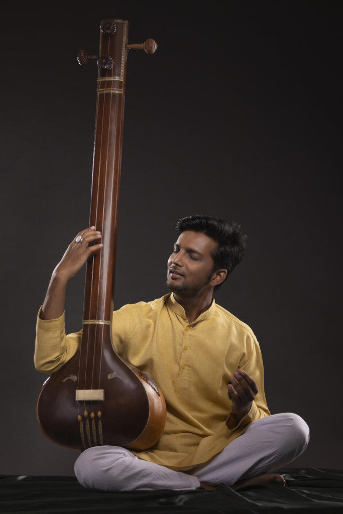 Portrait of young man performing with Tanpura at concert