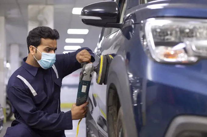 mechanic polishing a car with an electric orbital polisher in auto repair Shop