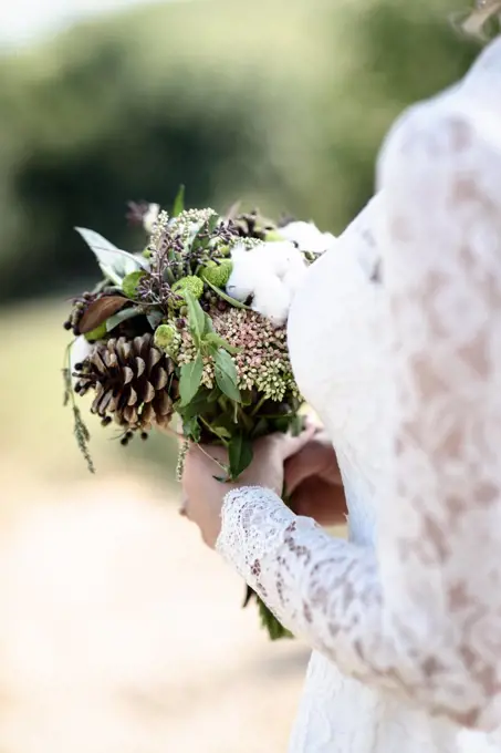 the bride's bouquet from cones and cotton close up in the hands of the bride lace dress forest backdrop