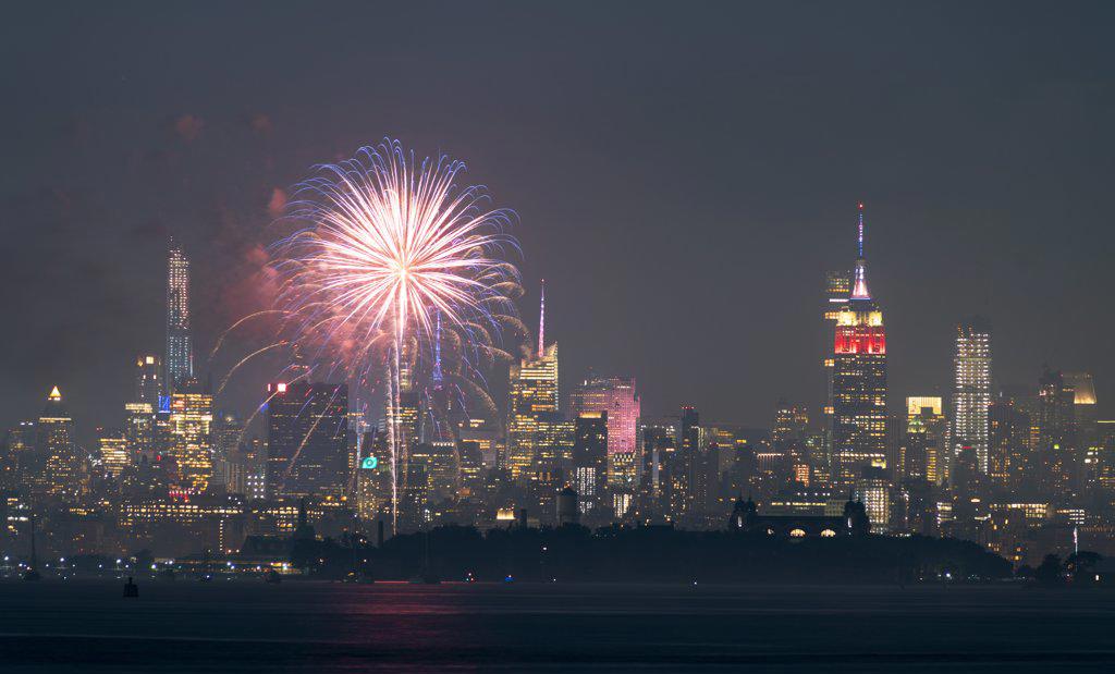 Fireworks are being set off from barges on the river between Jersey City and New York.