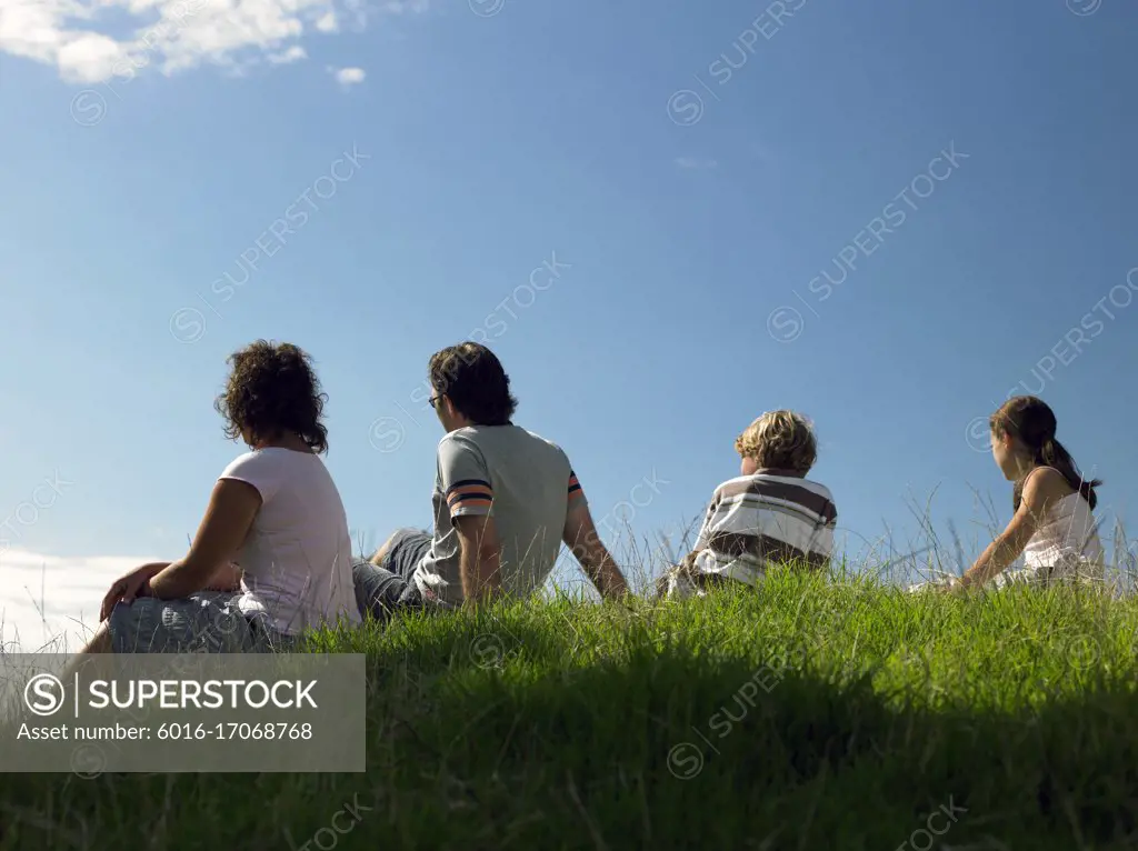 Back view of a group of young people sitting on top of a hill against blue sky
