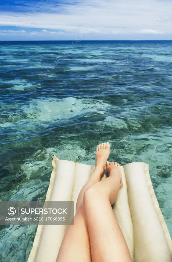 A close up view of legs and feet of a woman lying on lilo floating in tropical water